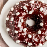 top down look at a chocolate bundt cake decorated with marshmallows and crushed peppermint candy. the cake is on a white plate.