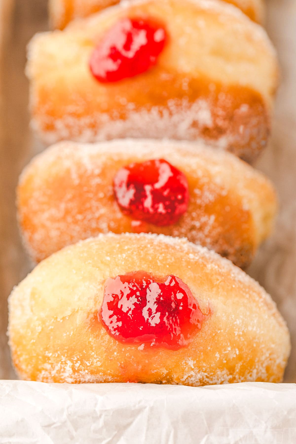 container with three jelly donuts rolled in sugar with red jam showing in the hole of the donut.