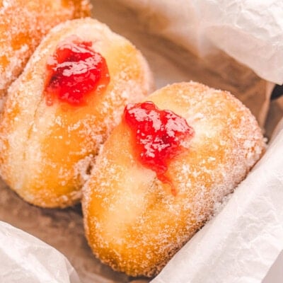 four sufganiyot donuts in a parchment lined container. the jelly is oozing out of the donuts.