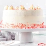 whole peppermint cake on a white cake stand with candy canes crumbles around the base.