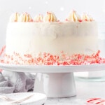 whole peppermint cake on a white cake stand with candy canes crumbles around the base.