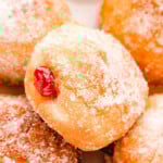 close up look at jelly filled donut rolled in sugar sitting on a layer of more jelly donuts.