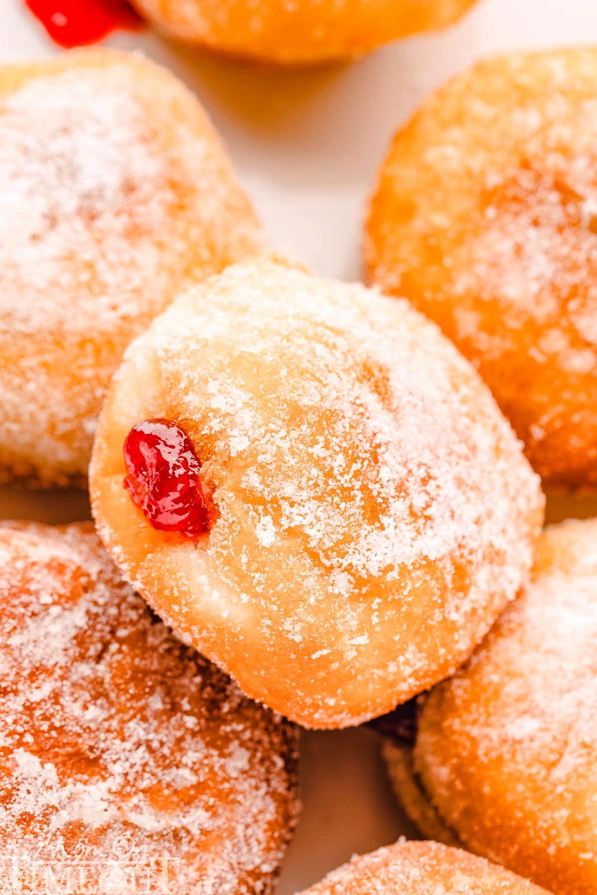 close up look at jelly filled donut rolled in sugar sitting on a layer of more jelly donuts.