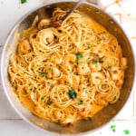 top down look at bang bang shrimp pasta recipe in a large skillet garnished with fresh parsley. skillet is sitting next to a white and orange kitchen towel.