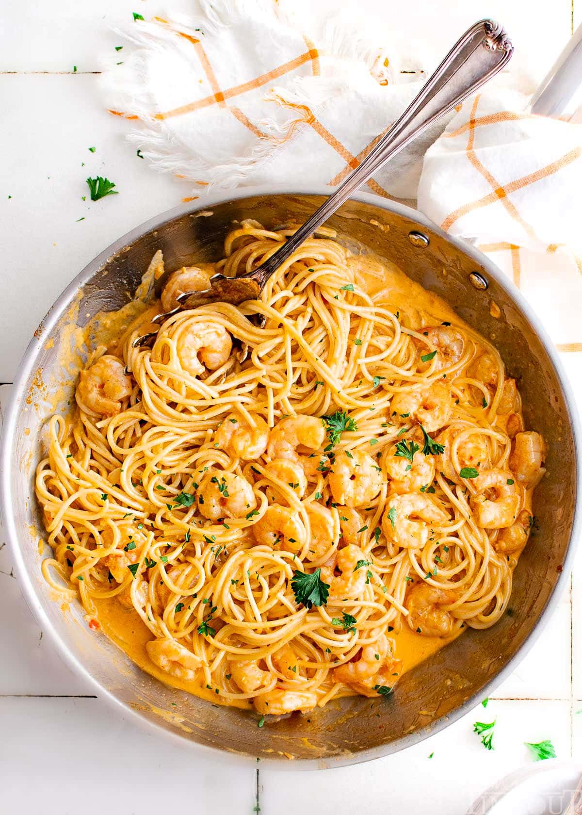 top down look at bang bang shrimp pasta recipe in a large skillet garnished with fresh parsley. skillet is sitting next to a white and orange kitchen towel. 