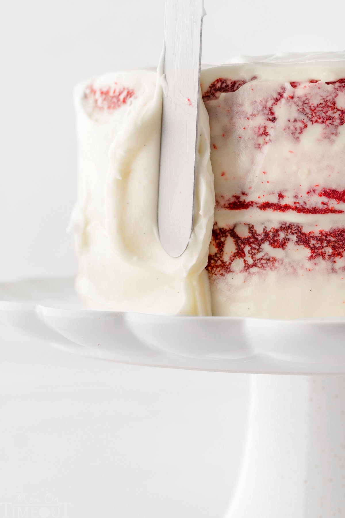 red velvet cake being frosted with cream cheese frosting using an offset spatula.