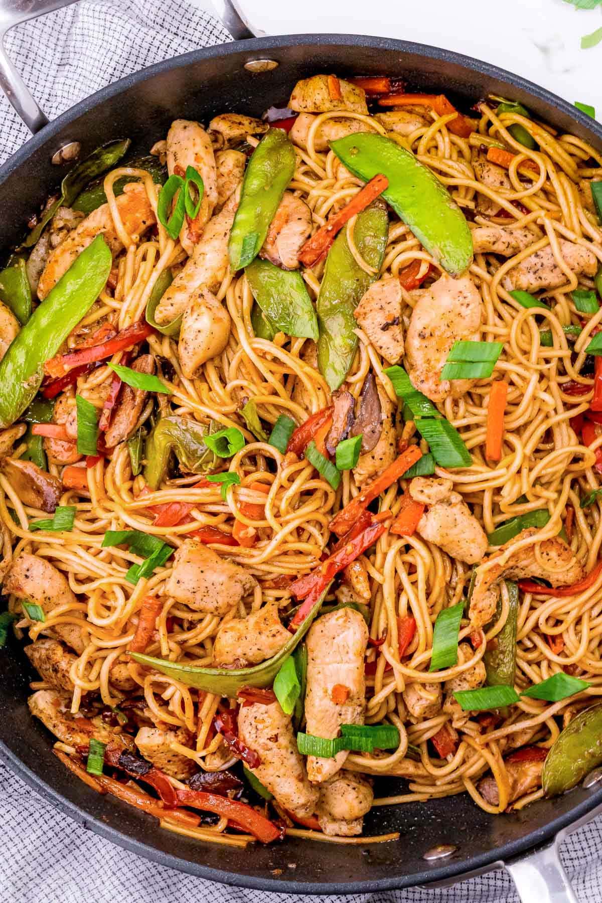 top down view of chicken lo mein in dark skillet. You can see an abundance of veggies and chicken mixed in with the lo mein noodles.
