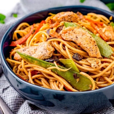 blue bowl filled with a generous serving of chicken lo mein made with snow peas and carrots.