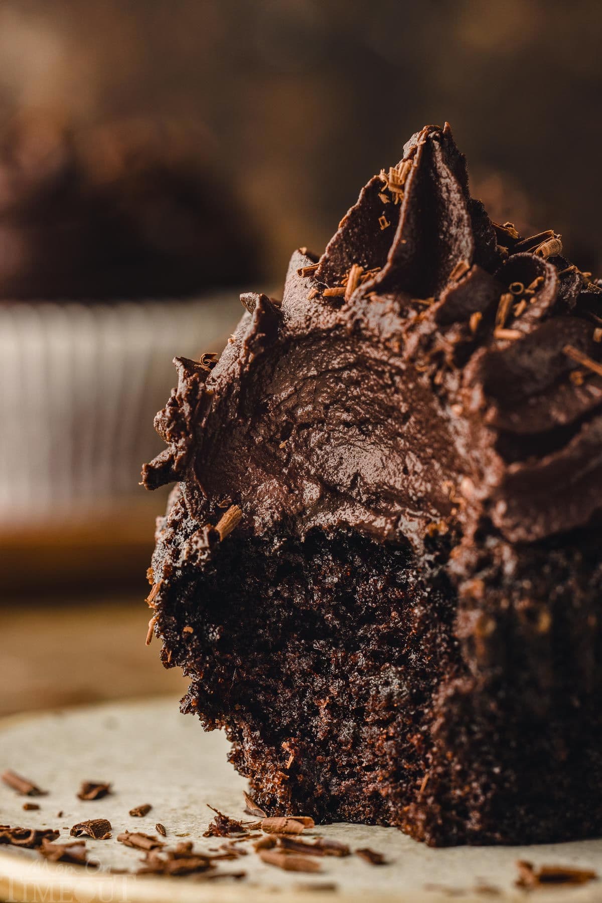 chocolate cupcake with bite taken out of it sitting on a small plate. the frosting is piled high on the cupcake and looks rich and creamy.