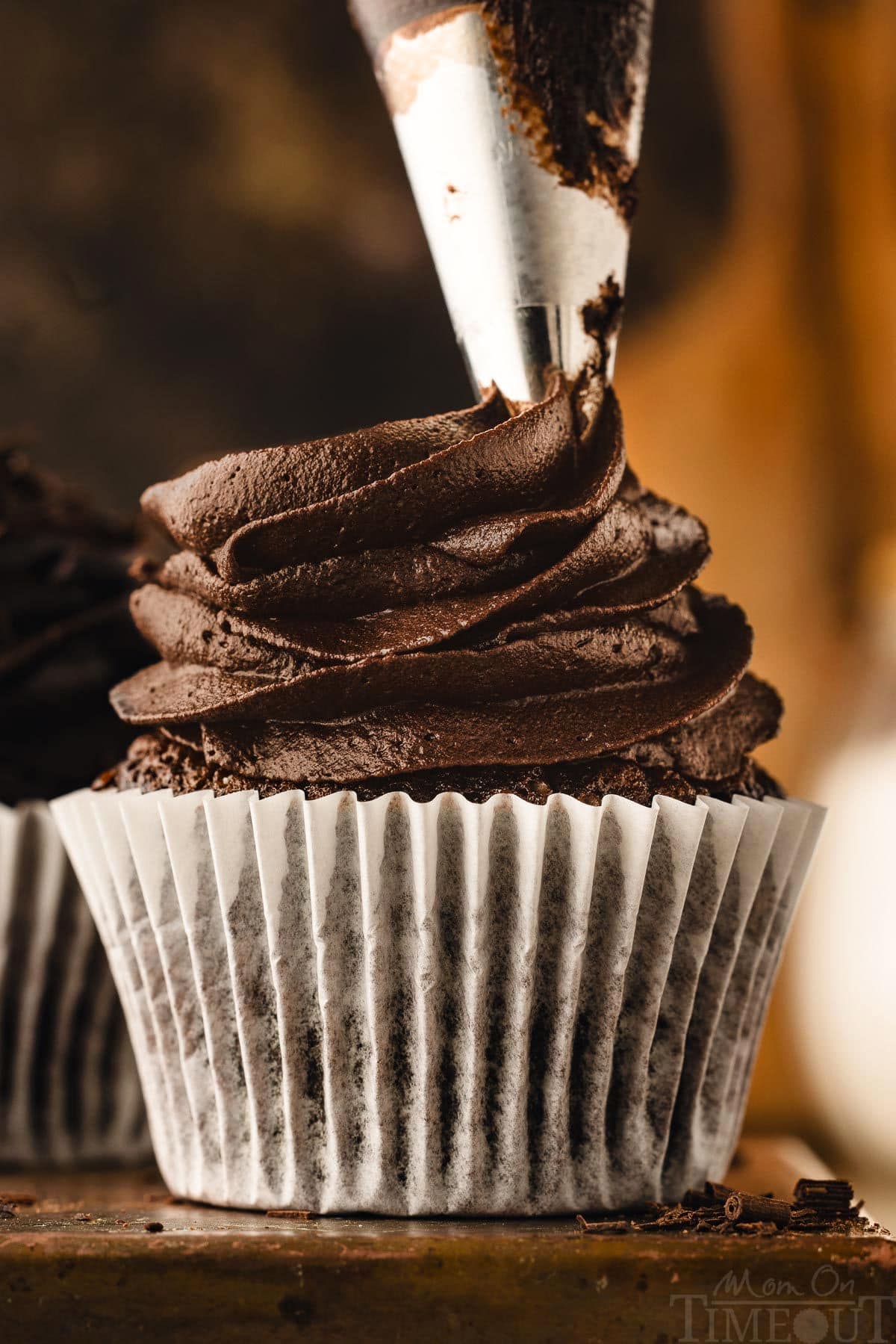 chocolate buttercream being piped onto a chocolate cupcake sitting on a dark metal surface.