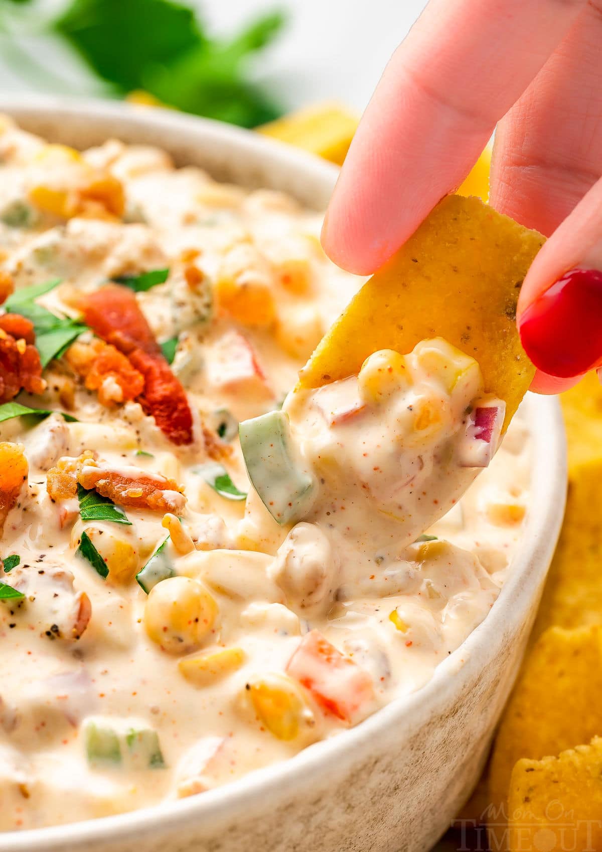 close up look at a frito scoop picking up a bit of corn dip from a small bowl. the dip has been topped with bacon and parsley.