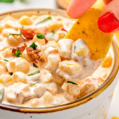 close up look at a frito scoop picking up a bit of corn dip from a small bowl. the dip has been topped with bacon and parsley.