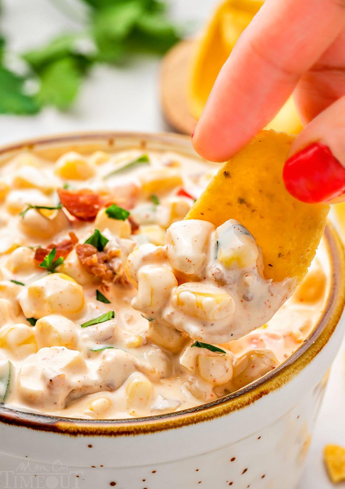 close up look at a frito scoop picking up a bit of corn dip from a small bowl. the dip has been topped with bacon and parsley. 