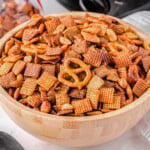 wood bowl in front of black slow cooker filled with chex mix.