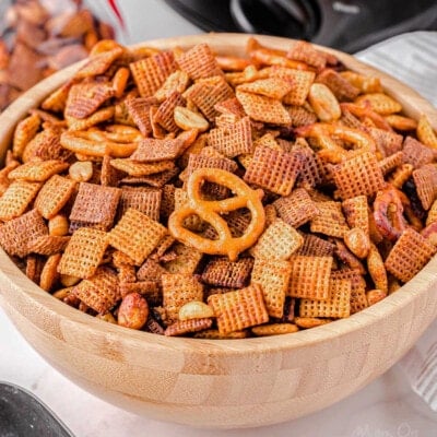 wood bowl in front of black slow cooker filled with chex mix.