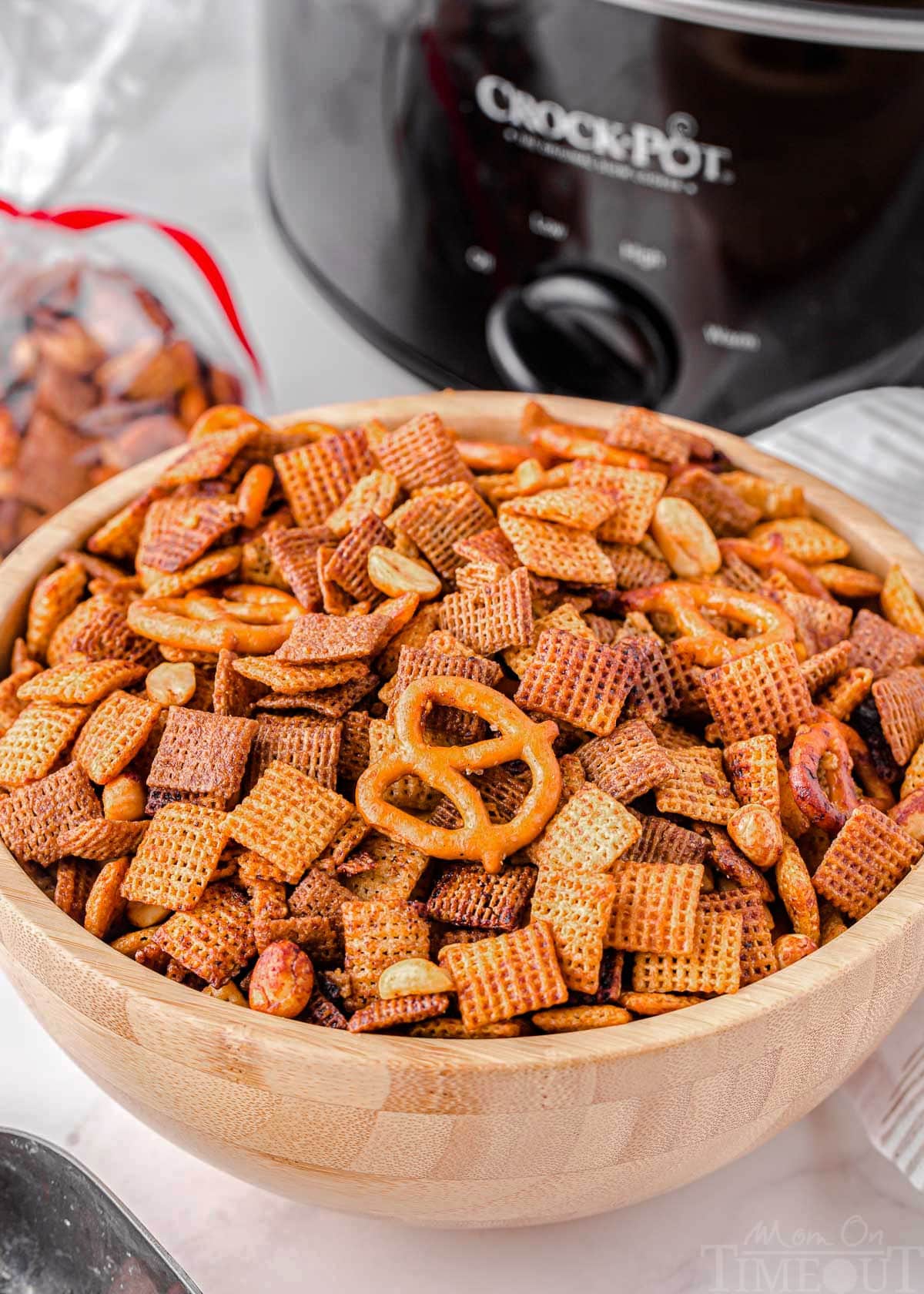 wood bowl in front of black slow cooker filled with chex mix.