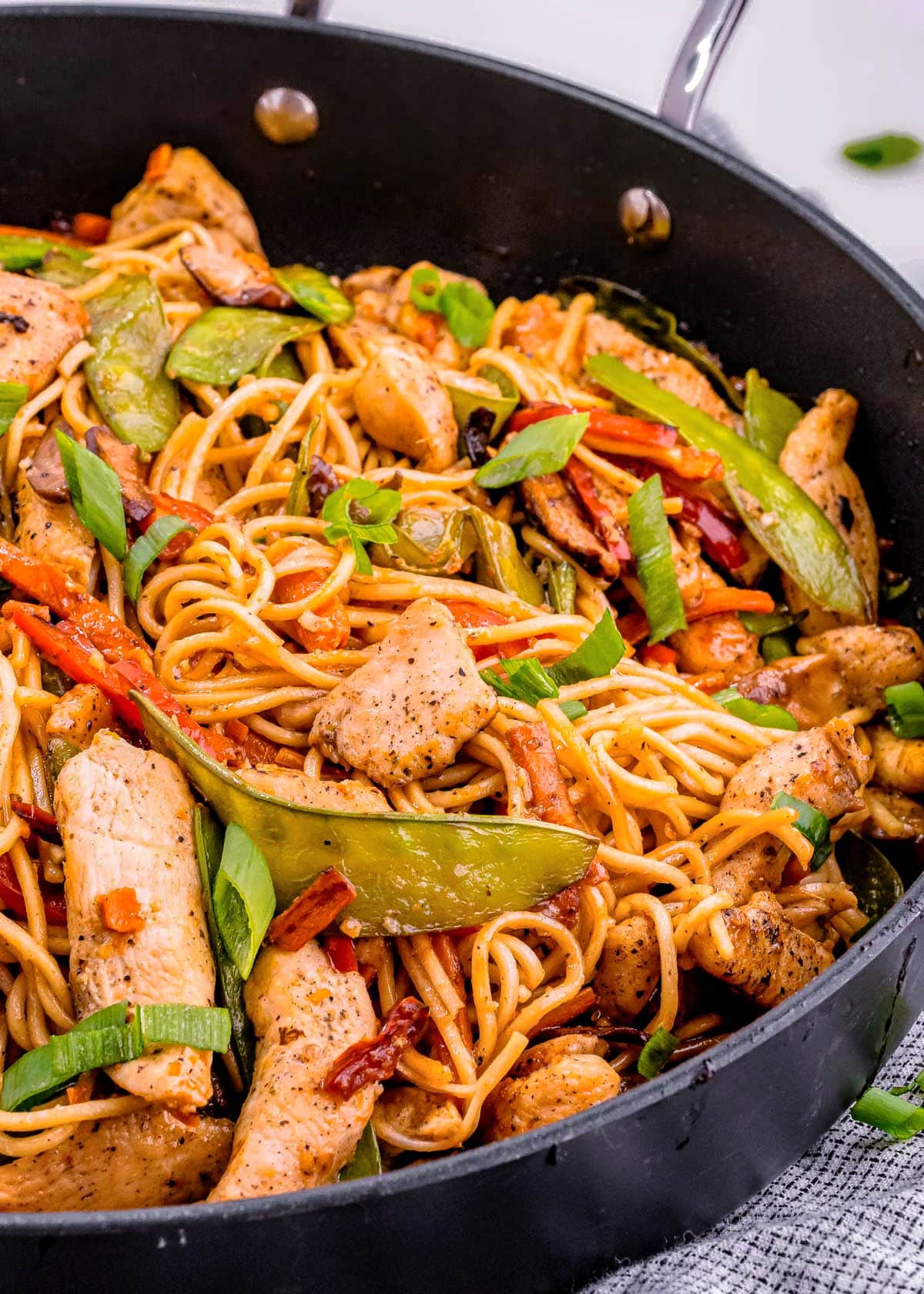 chicken lo mein in dark skillet. You can see an abundance of veggies and chicken mixed in with the lo mein noodles. Ready to be served.