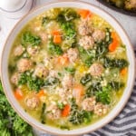 top down view of bowl of italian wedding soup topped with freshly grated parmesan cheese. the pot of soup is next to it.