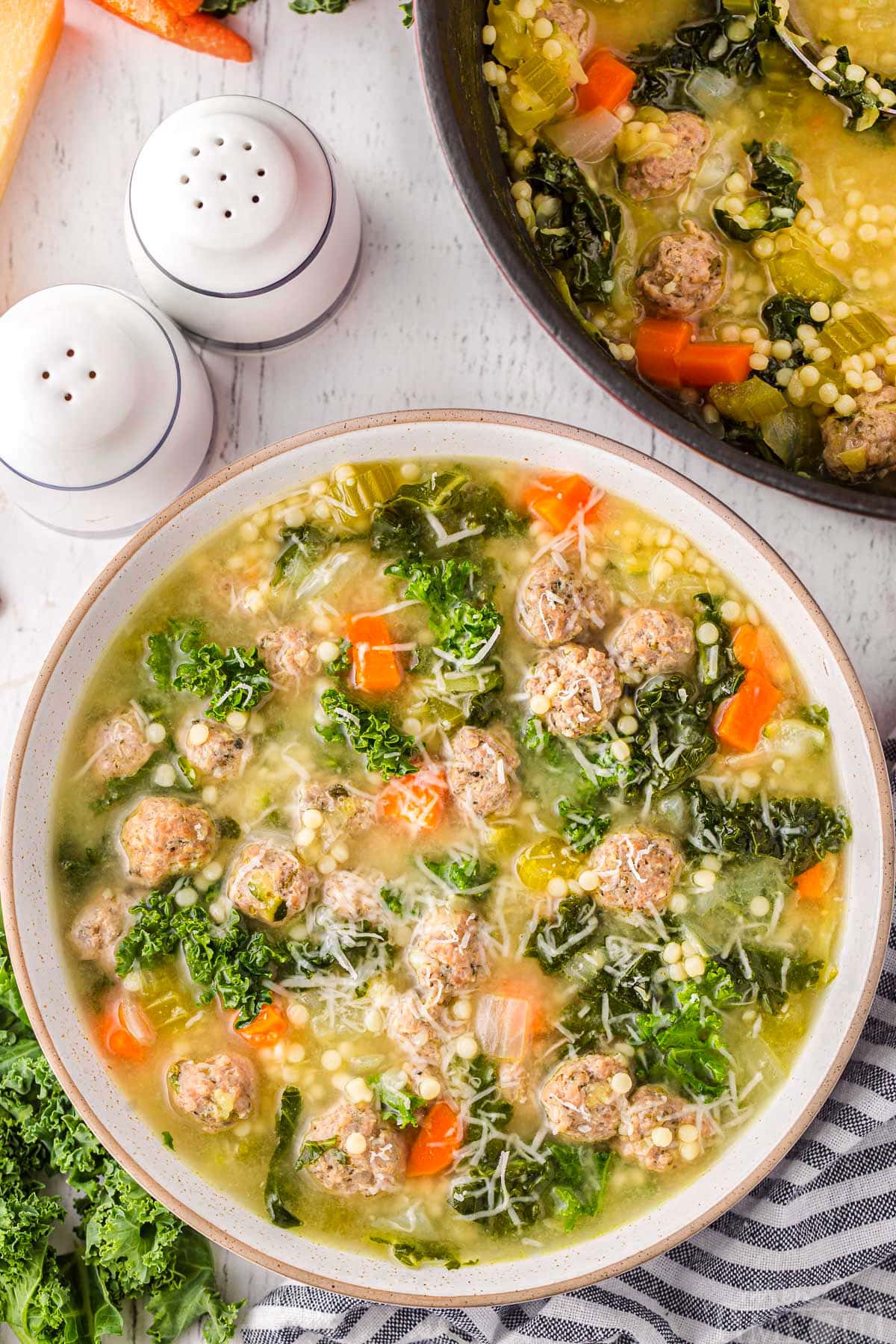 top down view of bowl of italian wedding soup topped with freshly grated parmesan cheese. the pot of soup is next to it.