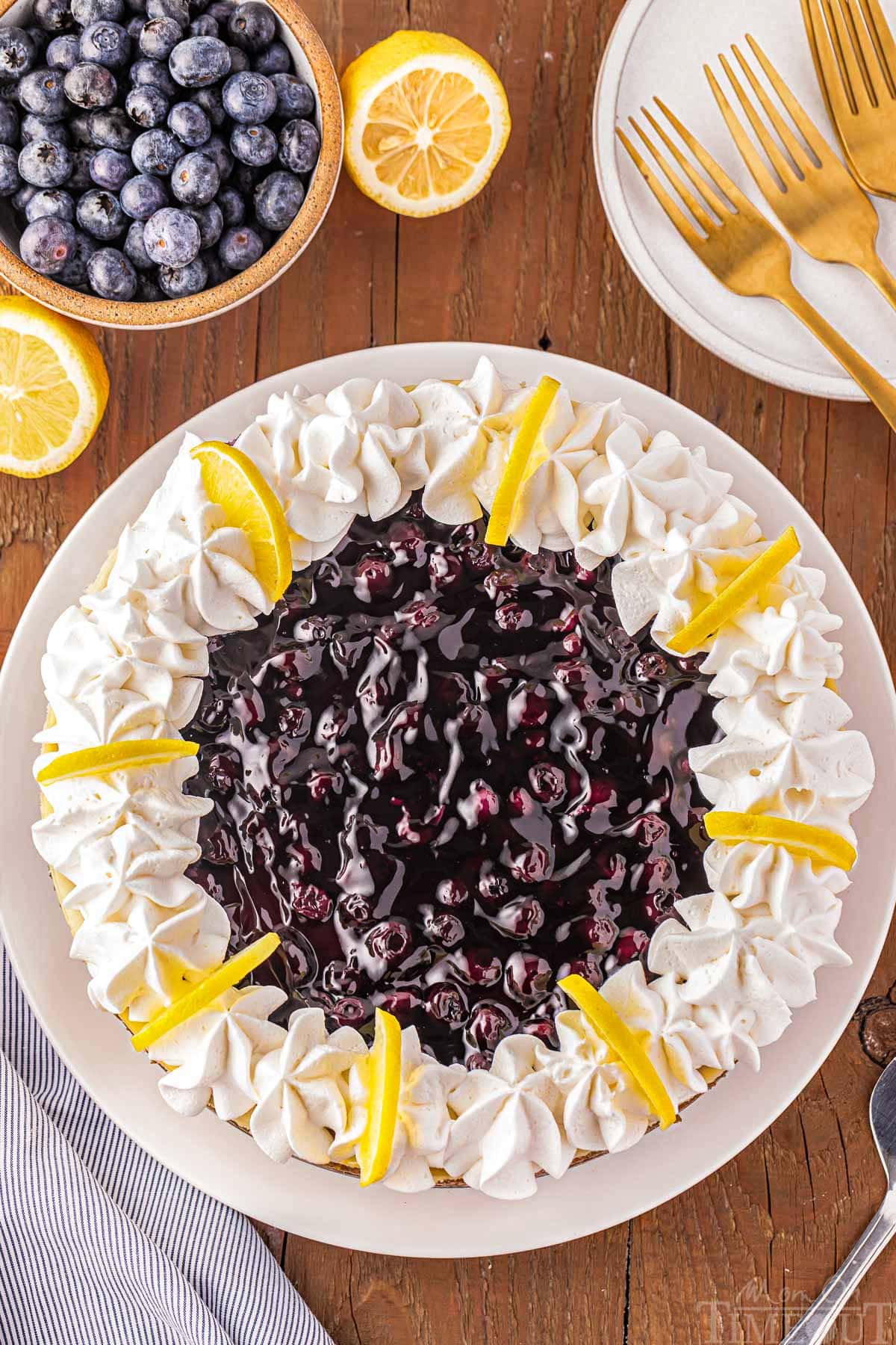 top down look at the blueberry pie filling on top of a lemon cheesecake. small bowl of blueberries next to the cheesecake.