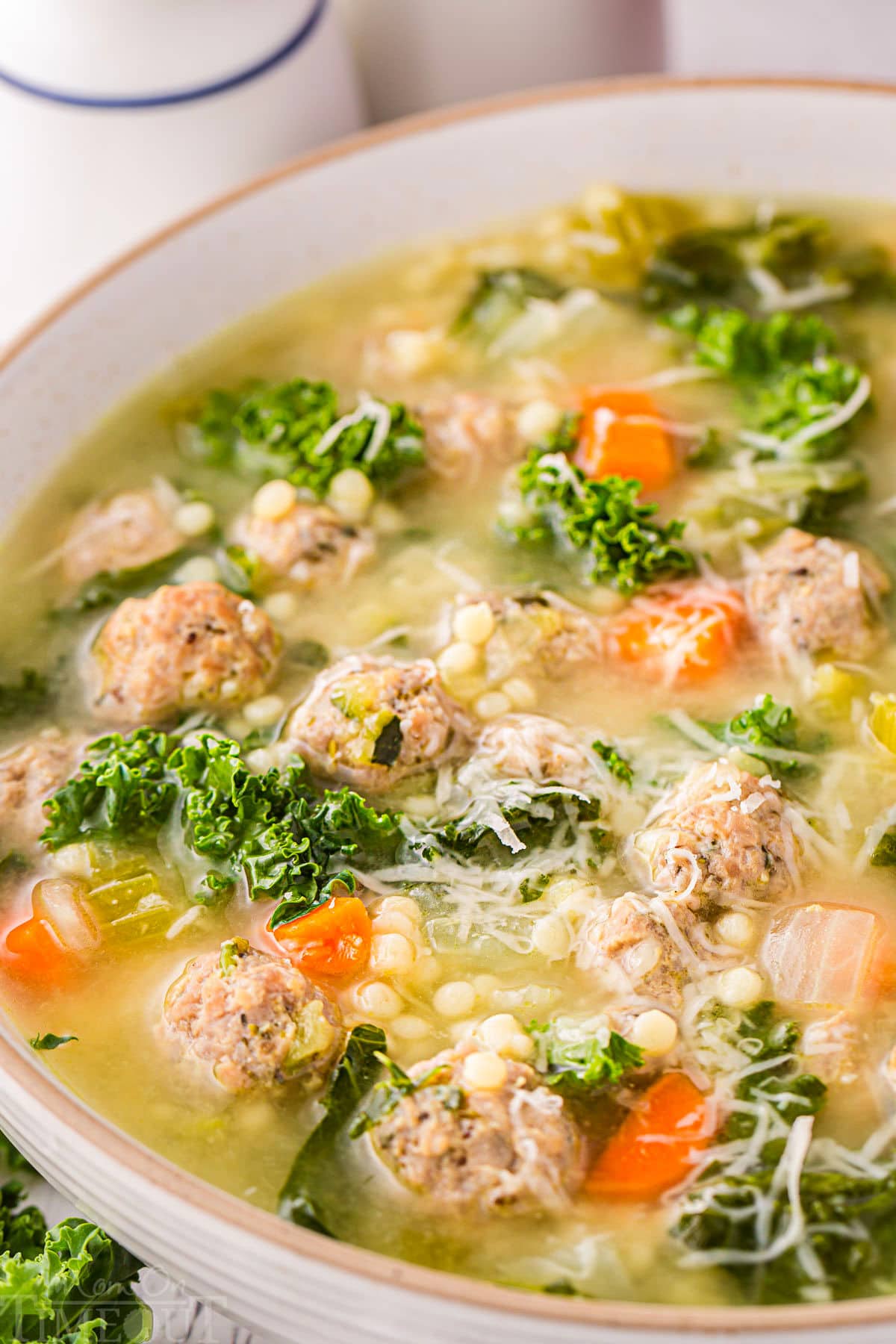 close up look at italian wedding soup in a round bowl. the soup has been topped with Parmesan cheese.