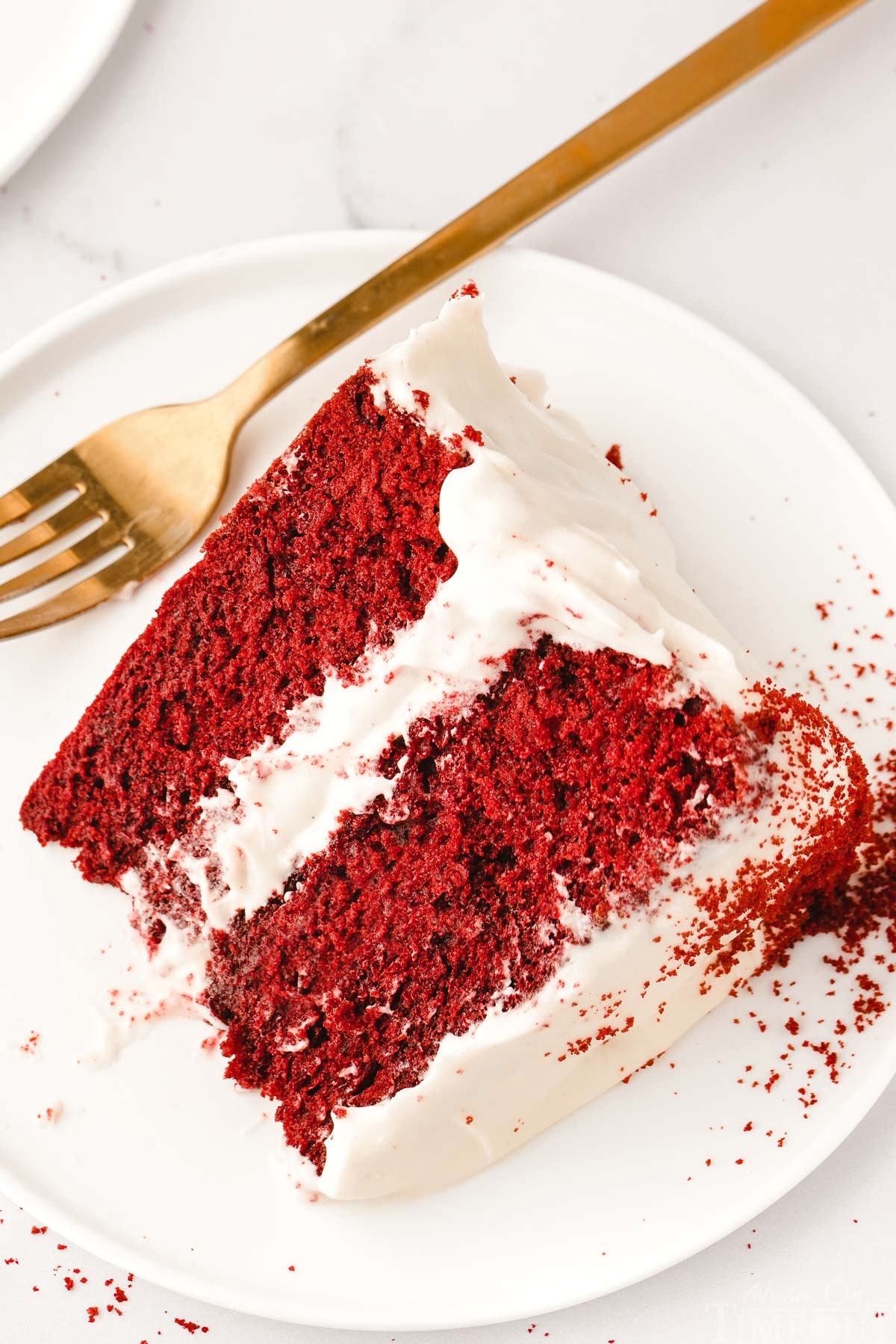 big slice of homemade red velvet cake with cream cheese frosting on small white round plate.