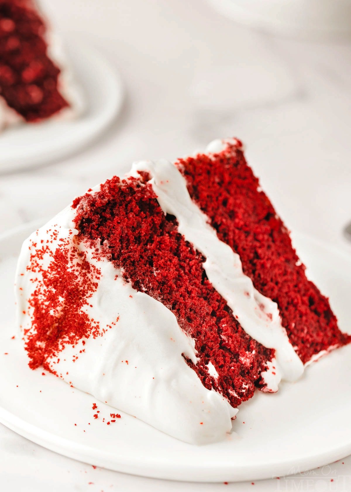 big slice of homemade red velvet cake with cream cheese frosting on small white round plate.