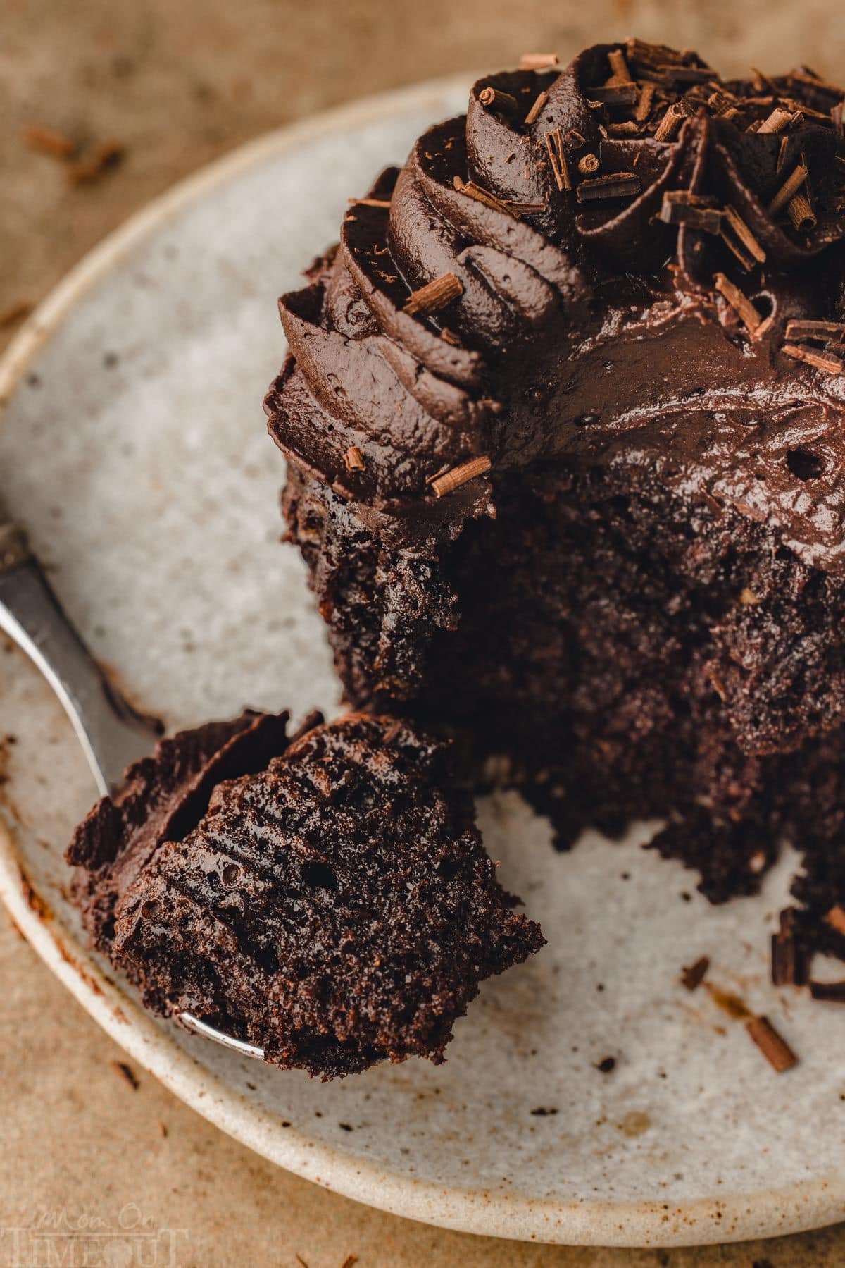 fork on plate next to chocolate cupcake with a bite of cupcake also on the fork. 