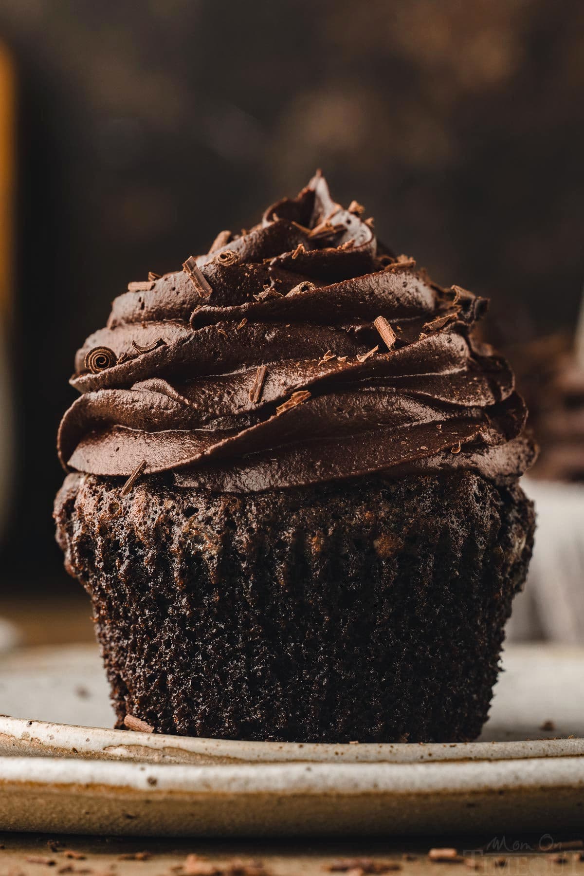 chocolate cupcake with liner removed sitting on white plate. cupcake has been topped with a chocolate buttercream frosting.