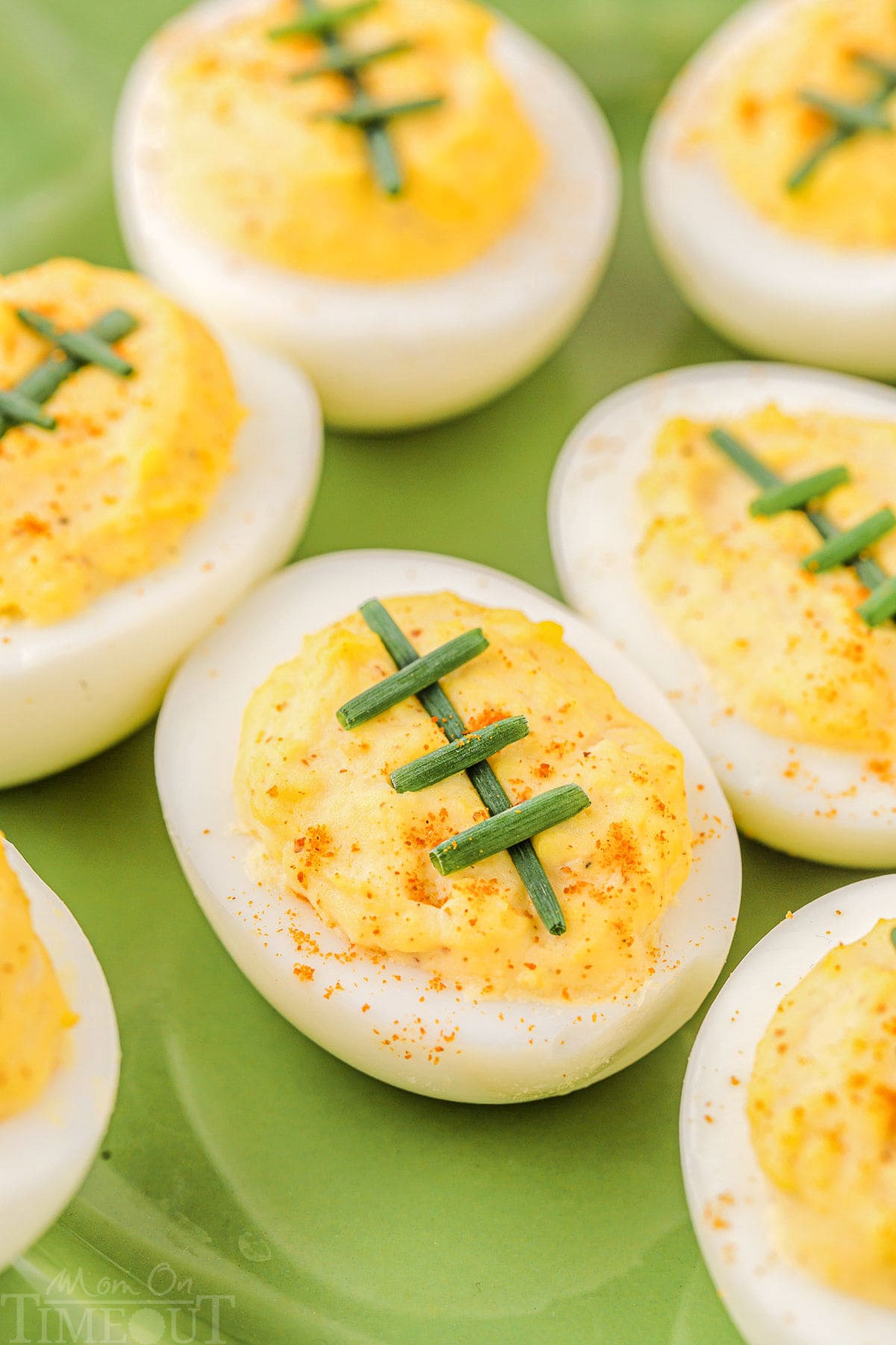 deviled eggs decorated to look like footballs with chives on a green plate.