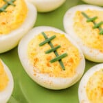 deviled eggs decorated to look like footballs with chives on a green plate.