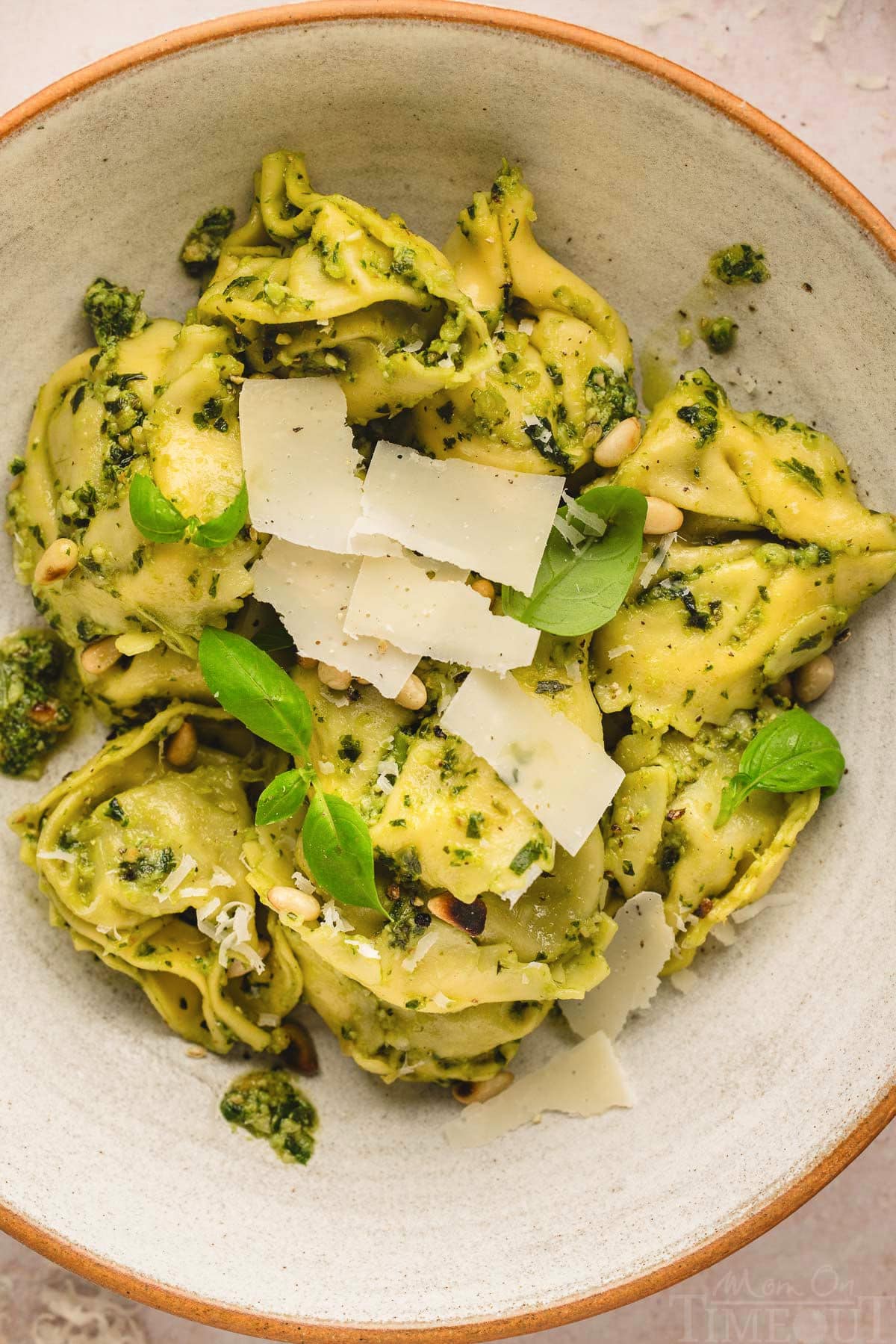 top down look at a bowl of pesto tortellini topped with fresh basil leaves and Parmesan cheese.