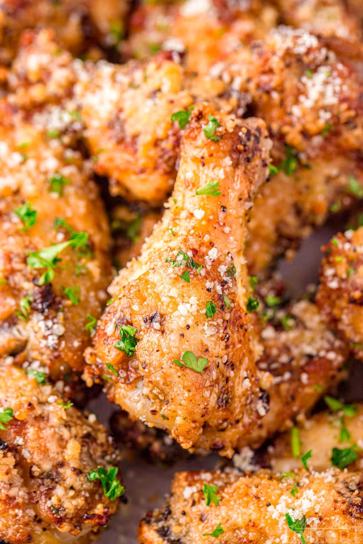 close up look at garlic parmesan chicken wings with a fresh dusting of parmesan cheese and parsley.