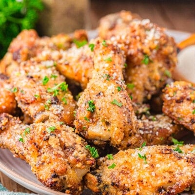 serving plate loaded with crispy golden garlic parmesan wings that have been garnished with fresh parsley.