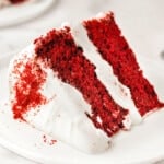 big slice of homemade red velvet cake with cream cheese frosting on small white round plate.