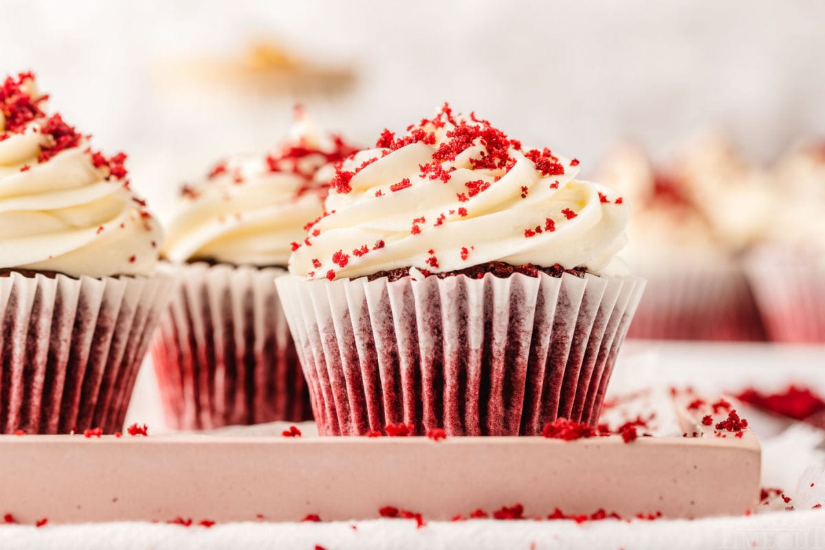 red velvet cupcakes on a pink tray frosted with cream cheese frosting and sprinkled with crumbs.