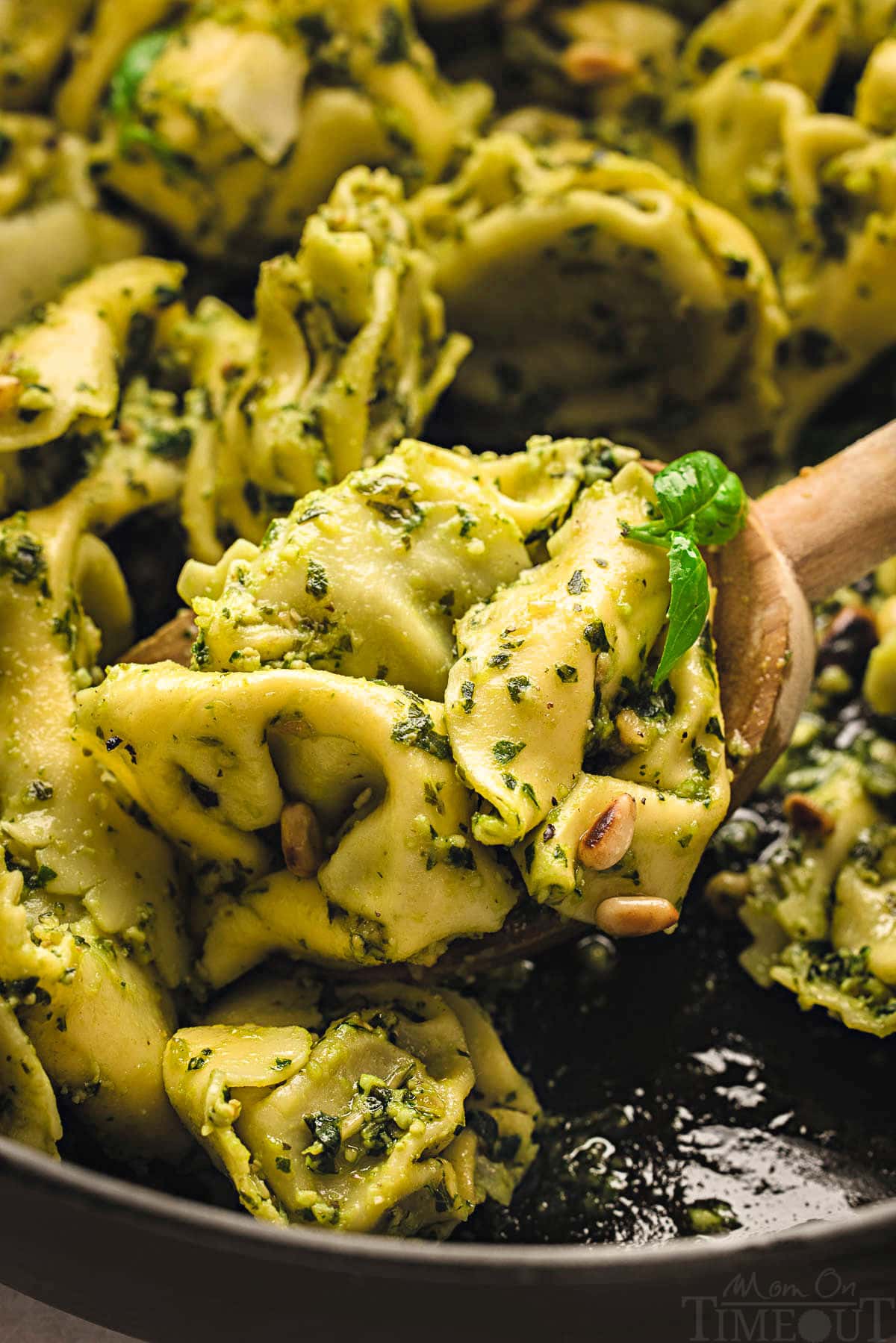 wooden spoon in cast iron skillet filled with tortellini pesto.
