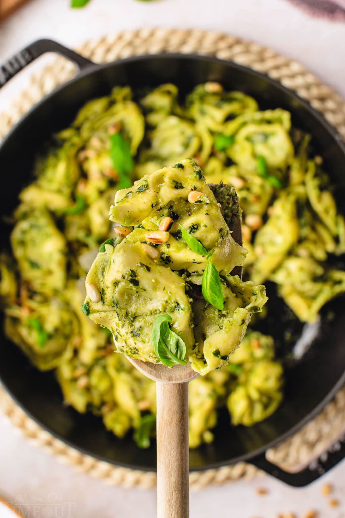 spoonful of pesto tortellini held over a cast iron skillet filled with the rest of the pasta.