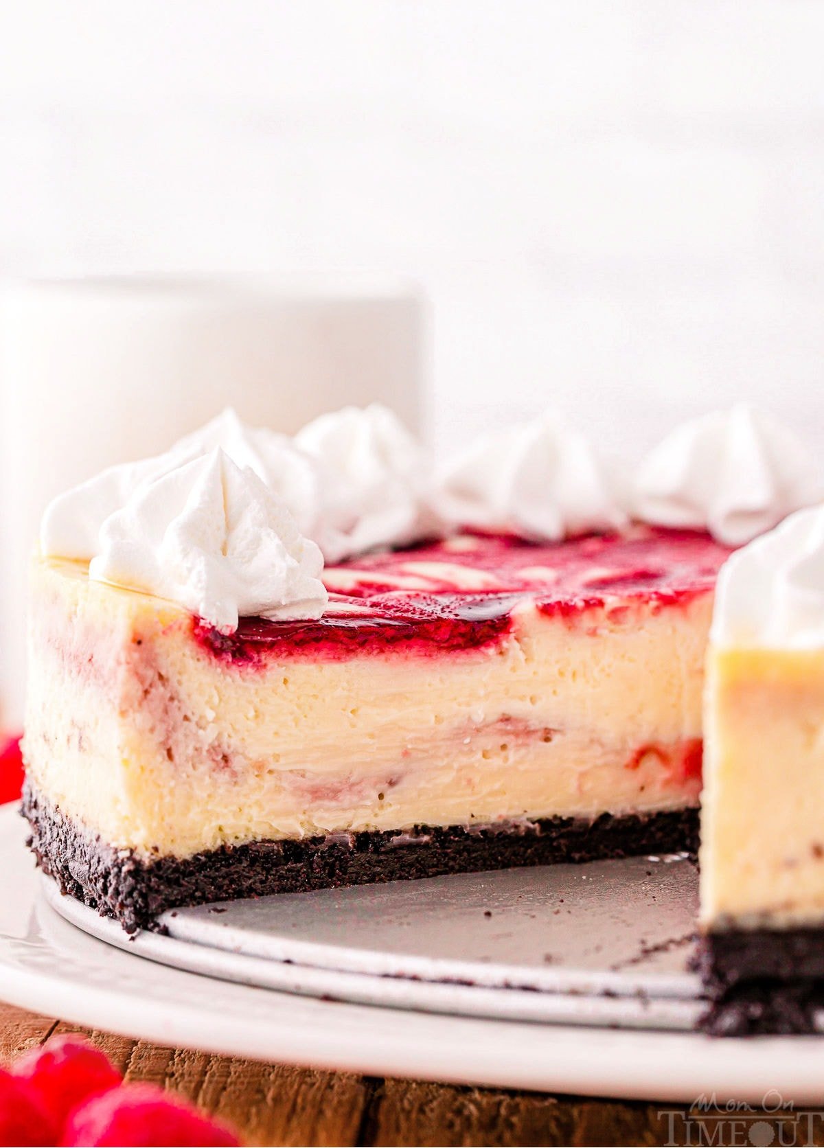 profile shot of white chocolate raspberry cheesecake with an OREO cheesecake topped with whipped cream.