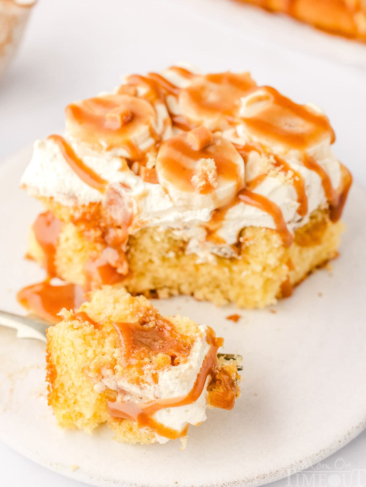 forkful of banoffee poke cake sitting next tot he rest of the piece of cake on a small, white round plate.