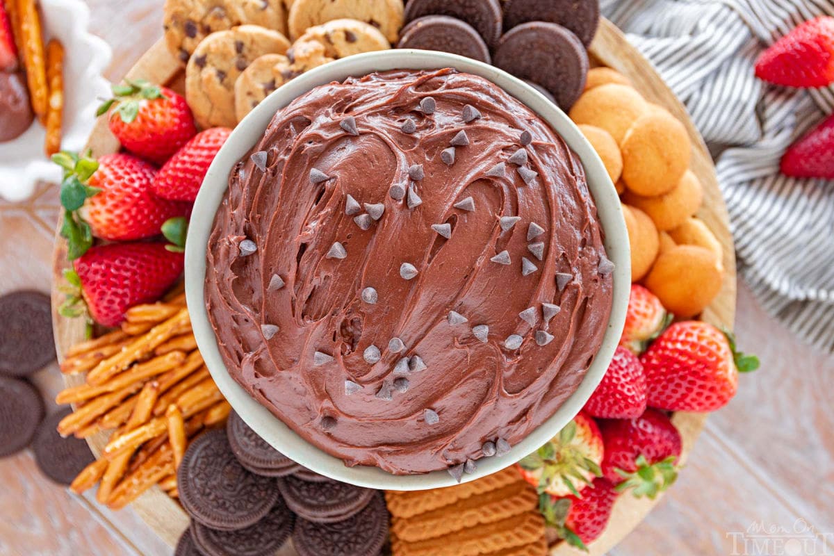 wide shot of top down look at edible brownie batter in serving bowl topped with mini chocolate chips surrounded by strawberries, pretzels, cookies and more dippers.