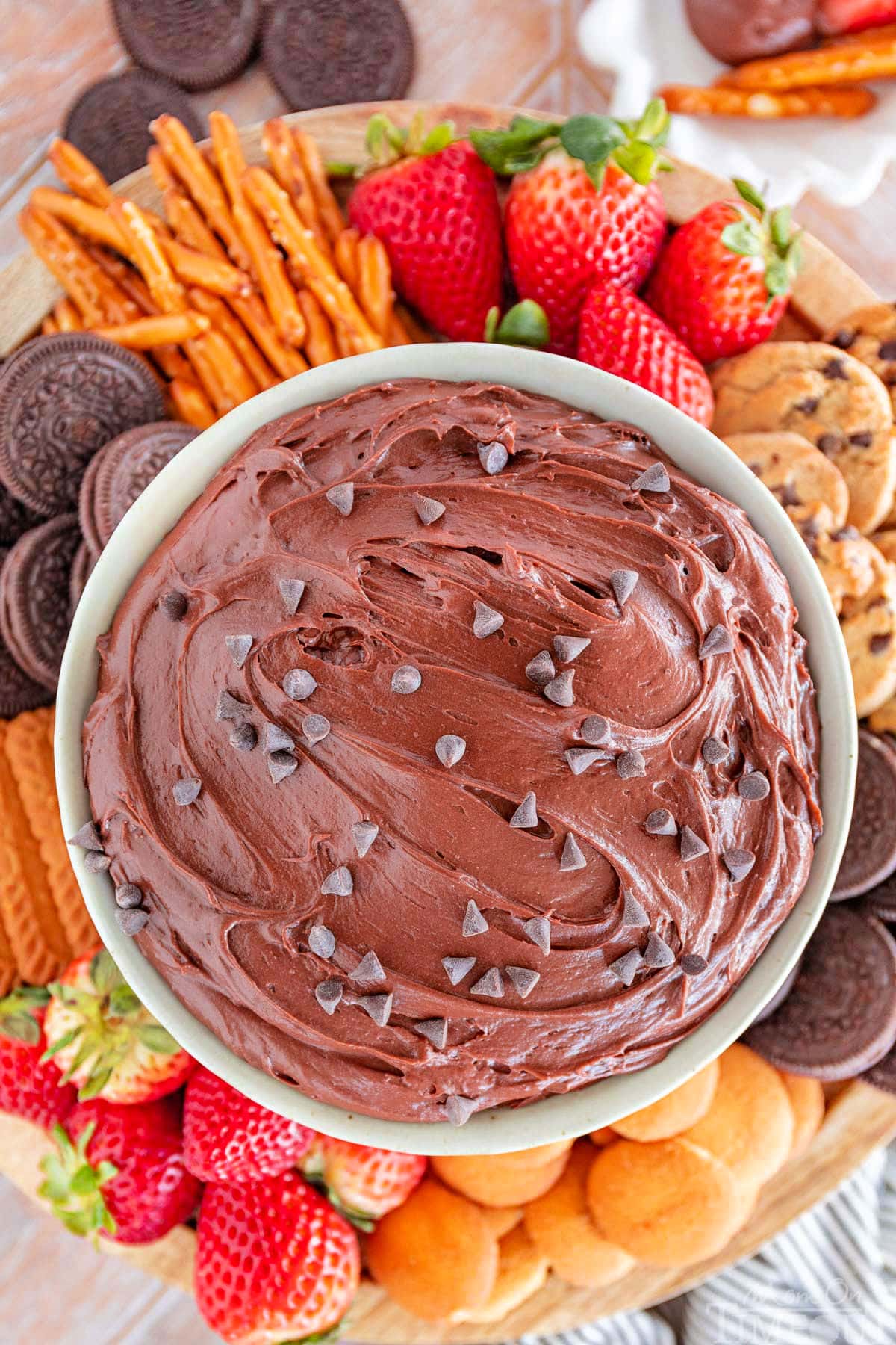 close up top down shot of a bowl of brownie batter dip surrounded by dippers including fresh strawberries, nilla wafers, pretzels and cookies.