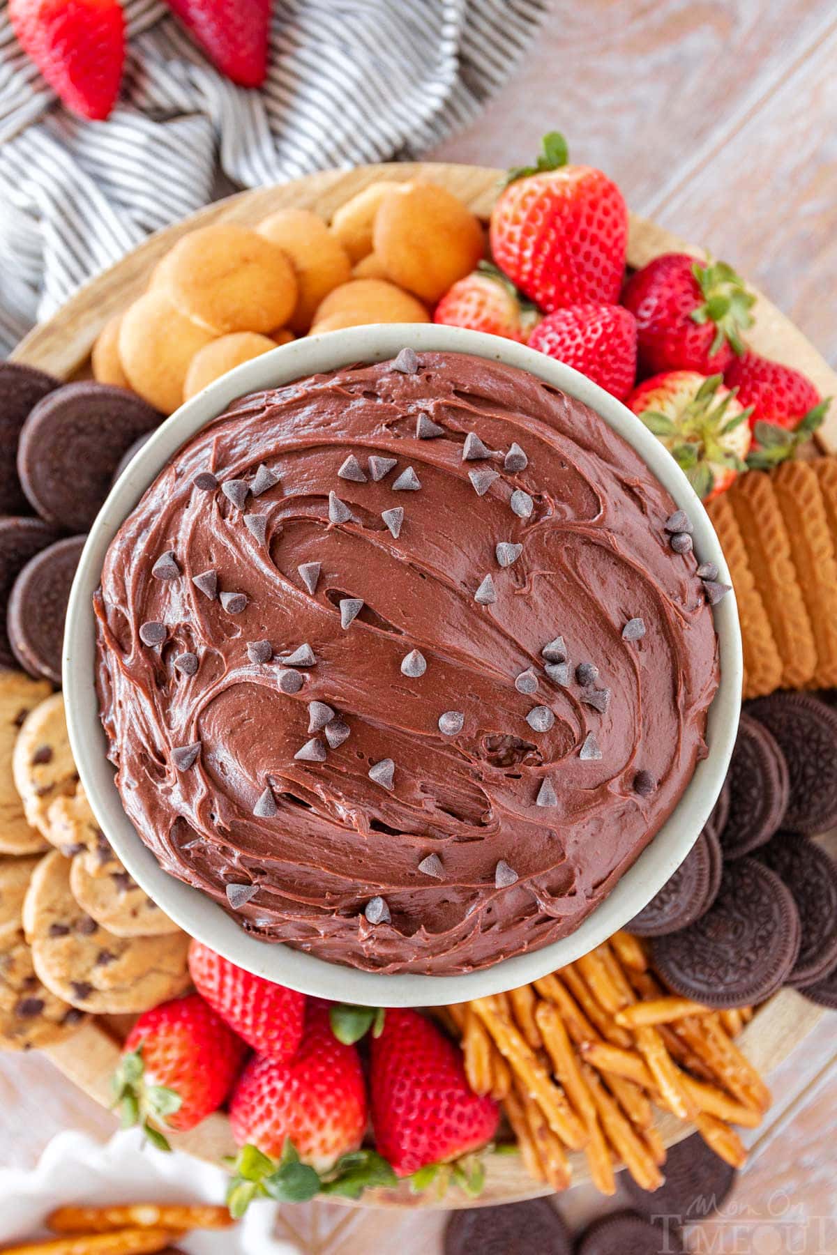 top down shot of a bowl of brownie batter dip surrounded by dippers including fresh strawberries, nilla wafers, pretzels and cookies.