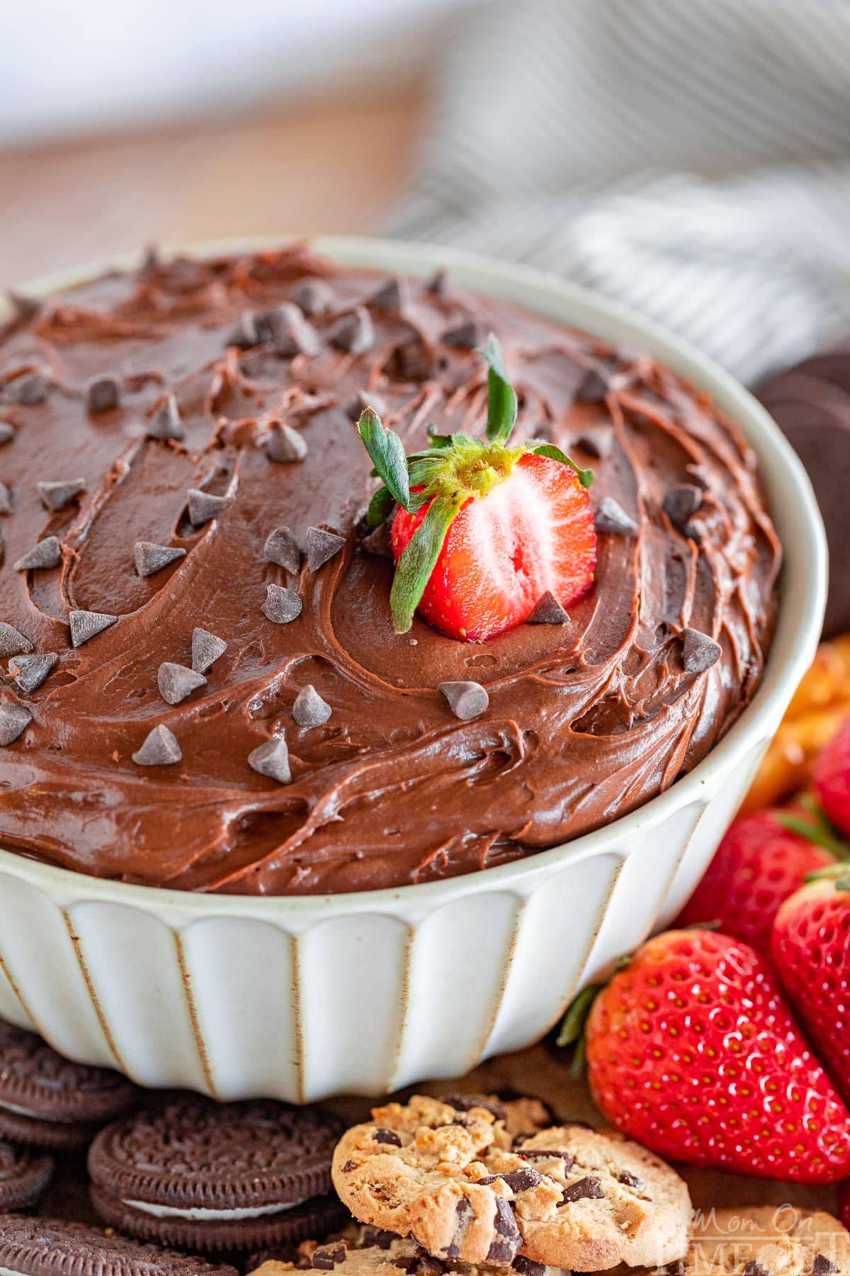 close up of bowl of brownie dip with a half strawberry stuck in the top along with a scattering of mini chocolate chips.