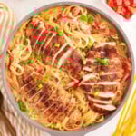 overhead shot of cajun chicken pasta still in the skillet ready to be served. the dish has been garnished with green onions and diced tomatoes.