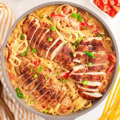 overhead shot of cajun chicken pasta still in the skillet ready to be served. the dish has been garnished with green onions and diced tomatoes.