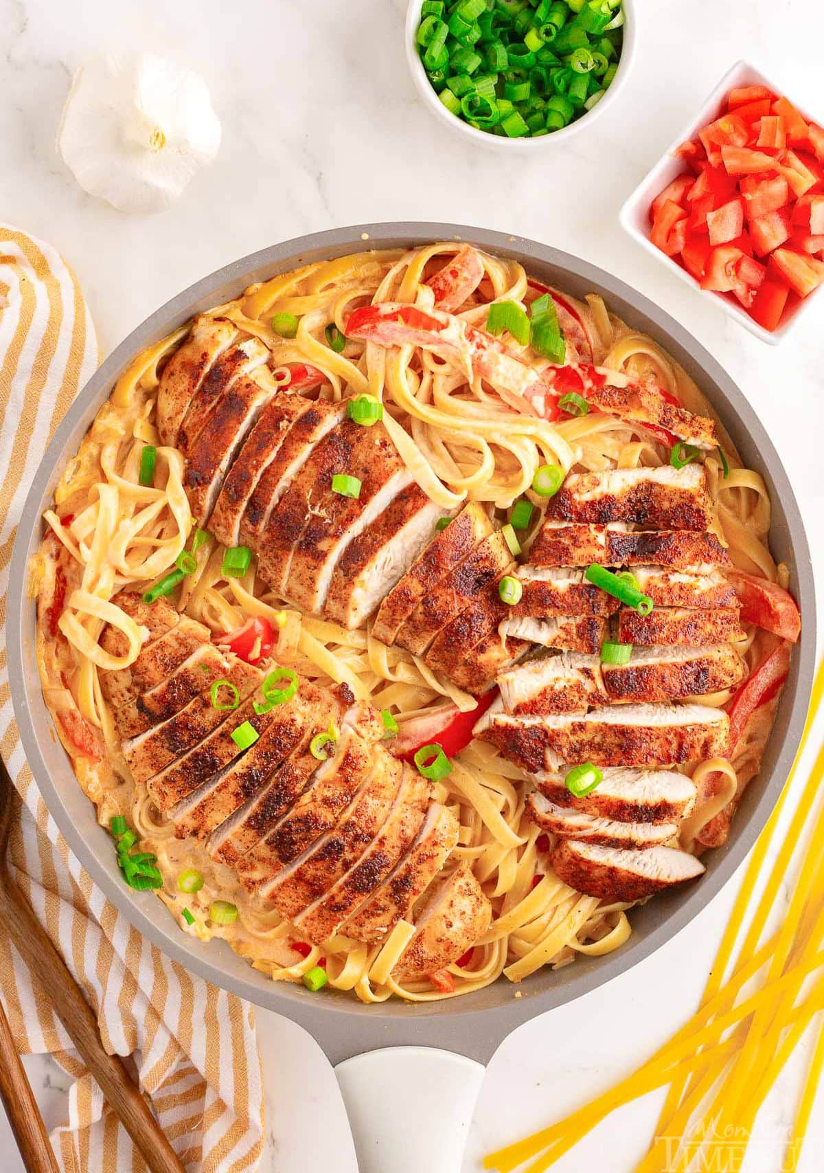 overhead shot of cajun chicken pasta still in the skillet ready to be served. the dish has been garnished with green onions and diced tomatoes.