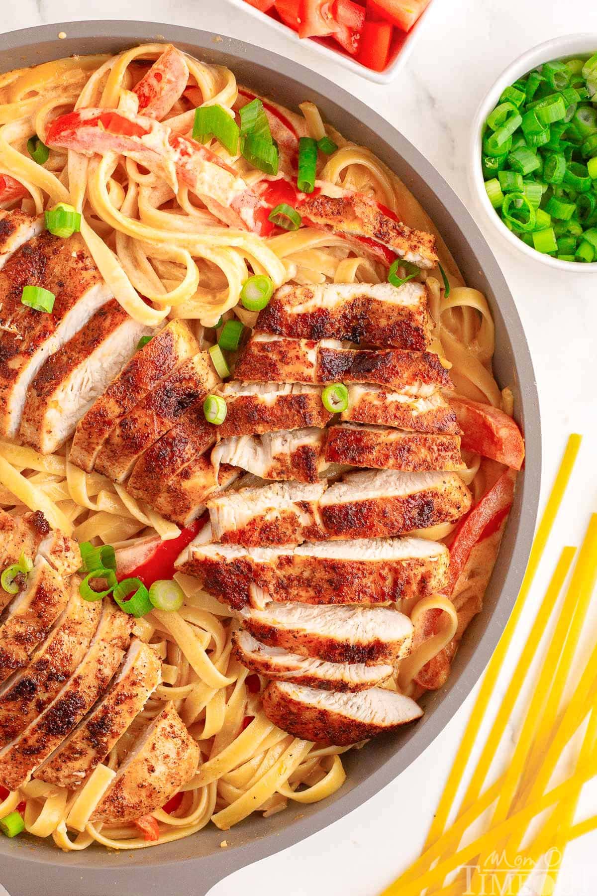 close up at cajun chicken pasta still in the skillet ready to be served. the dish has been garnished with green onions and diced tomatoes.