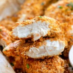 cornflake chicken in a pile with ranch dipping sauce. Top chicken tender is cut in half and stacked on each other showing the moist chicken and flavorful cornflake coating.