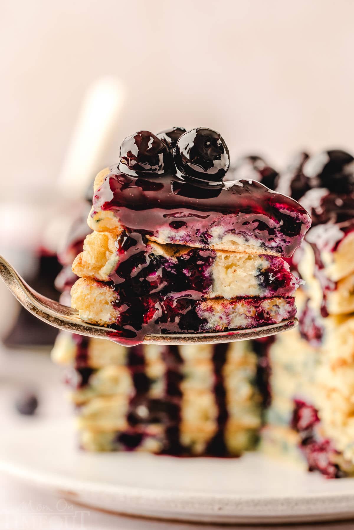 forkful of pancakes lifted in front of plate with lemon ricotta pancakes topped with a blueberry sauce.